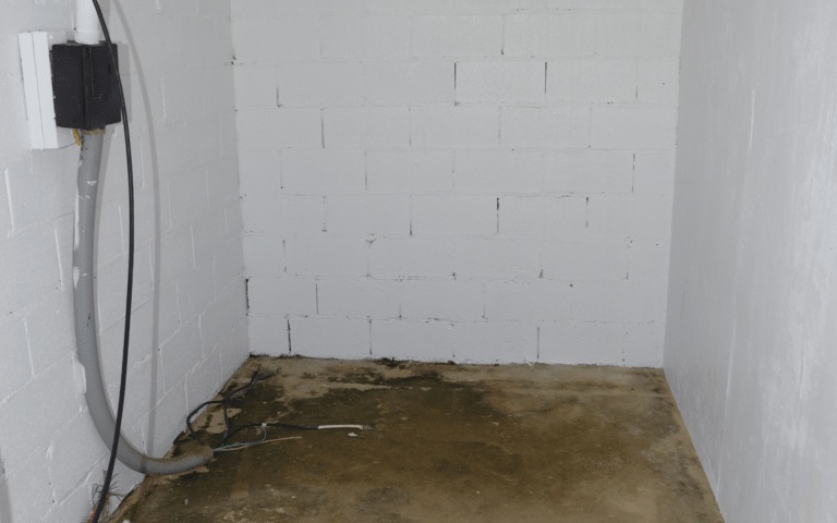 An empty basement with white painted cinder block walls and a bare concrete floor stained with water marks along the base of the wall