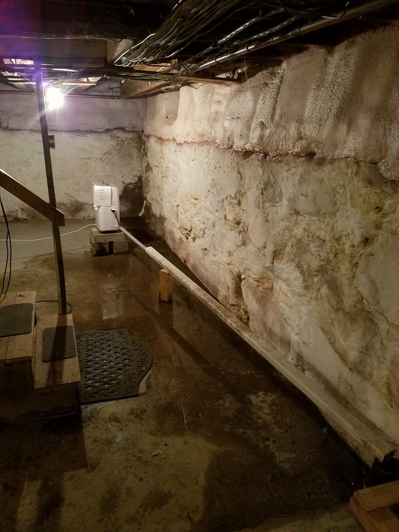 Eau stagnante sur le sol d’une cave à côté d’un mur de fondation en pierre brute, sous les solives du plancher