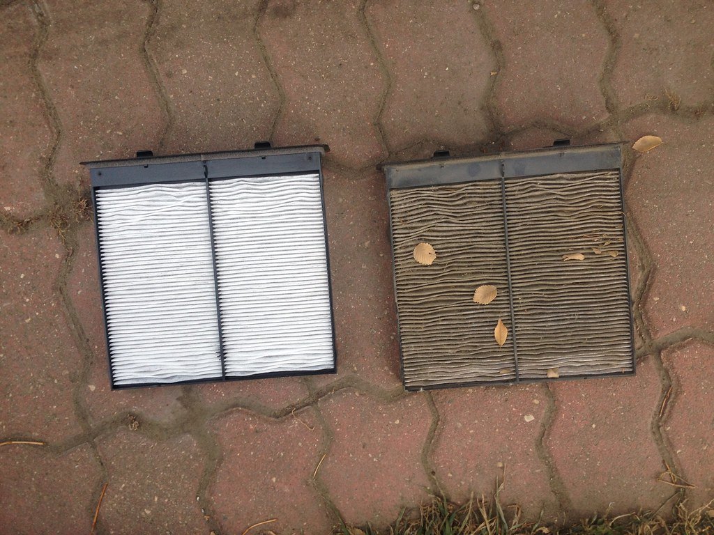 A clean white cabin air filter beside an old grey filter clogged with dirt and leaves