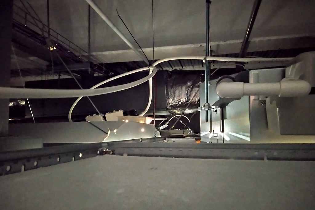 Ductwork and an air handling box running through a dark ceiling void above a suspended ceiling