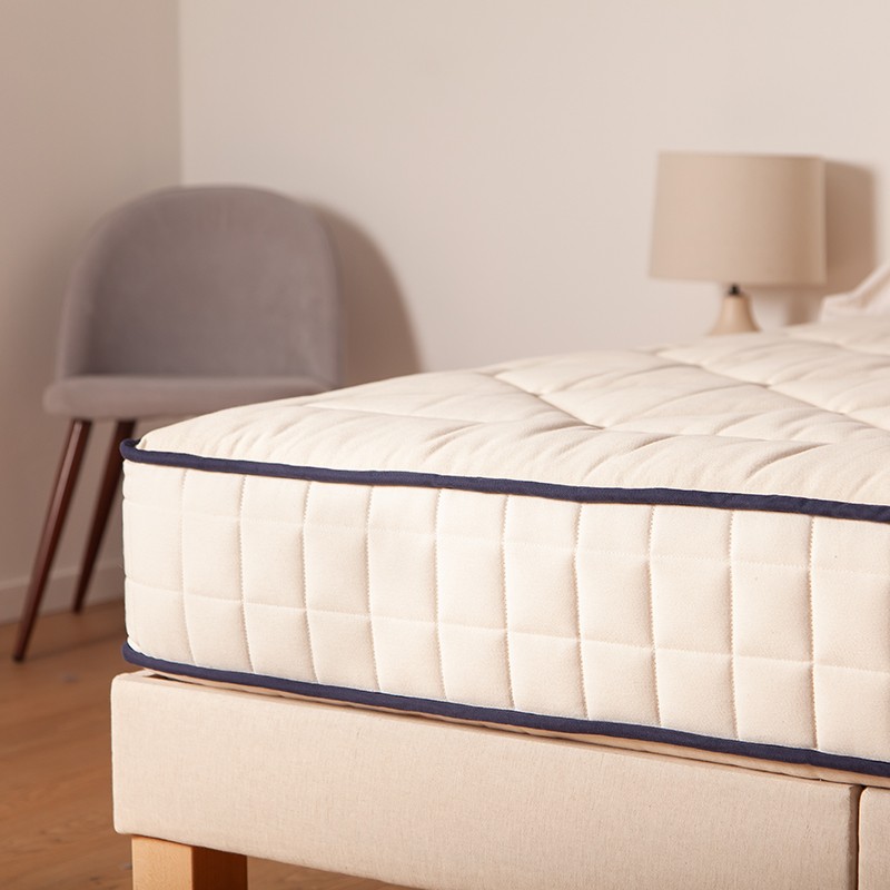 Colchón de látex natural Cosme sobre una base tapizada en un dormitorio luminoso