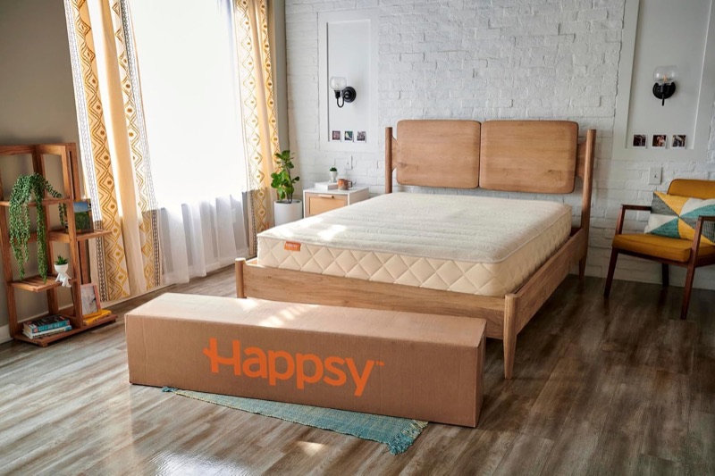 Happsy organic hybrid mattress on a wooden bed frame with its shipping box in front